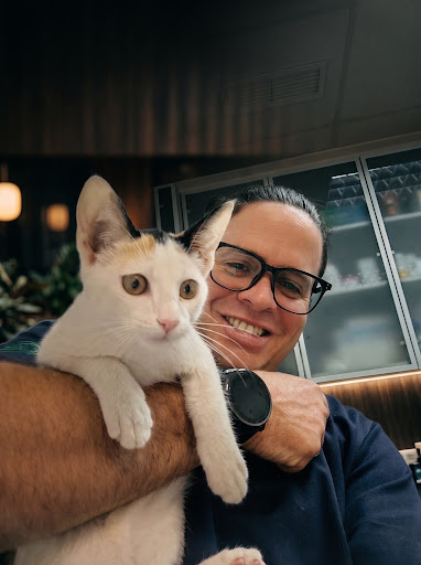 Dr. Yoenier Pérez sosteniendo con calidez y cercanía a un gato blanco y calicó en consulta